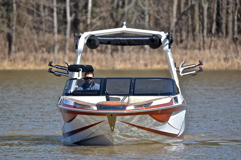Slide: The Image of 2023 Centurion Ri230 boat cruising on a lake with a driver, surrounded by trees. - 11