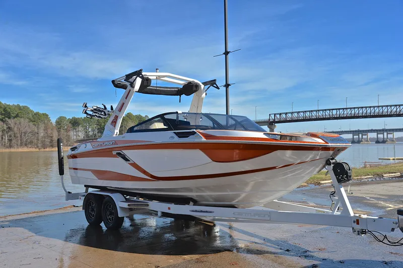Slide: The Image of 2023 Centurion Ri230 boat on trailer by a lake with bridge in background. - 18
