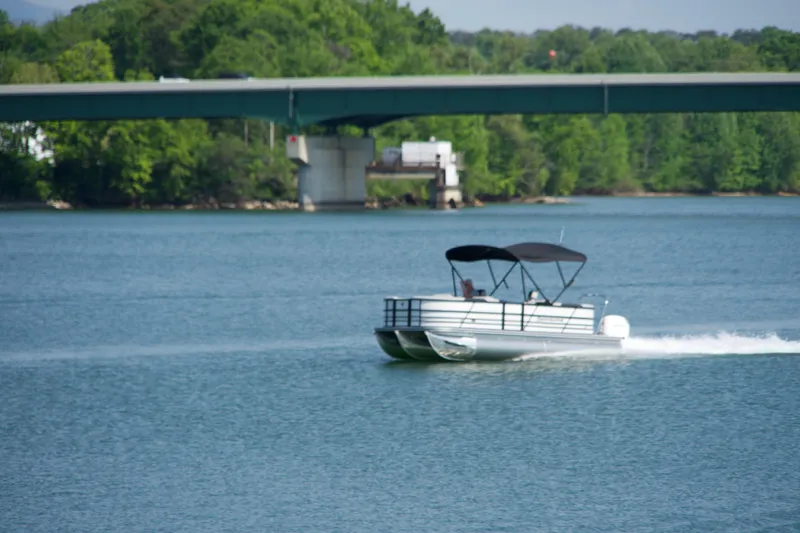 Slide: The Image of 2026 Berkshire 22 RFX LE pontoon boat cruising on a scenic lake near a bridge. - 22