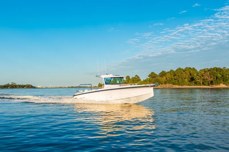 The Image of 2026 Axopar 29 CCX cruising on a serene lake with a forested shoreline. - 2