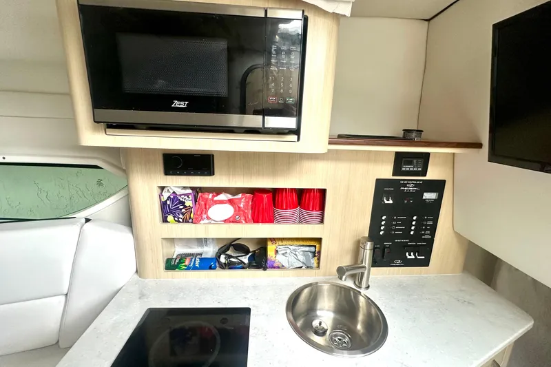 Slide: The Image of 2025 Regal 26 XO boat kitchenette with microwave, sink, and storage shelves. - 44