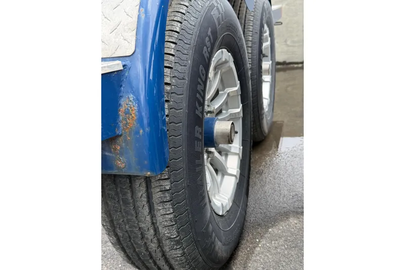 Slide: The Image of Trailer tire of a 2022 Crownline 255 SS SURF boat, showing rust on blue fender. - 44