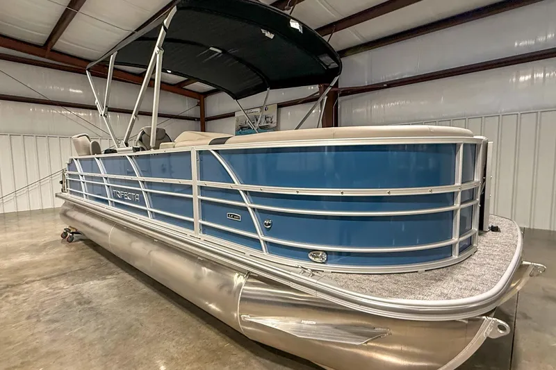 Slide: The Image of 2025 Trifecta 24TRFC LE pontoon boat in a warehouse, featuring blue siding and a black canopy. - 3