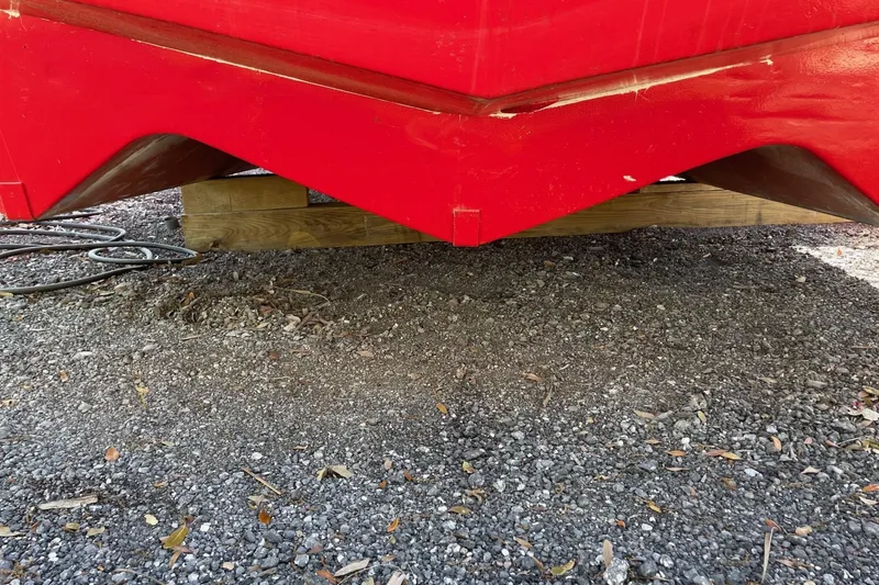 Slide: The Image of Red 1987 Commercial Buoy Tender hull resting on wooden supports, gravel ground. - 4