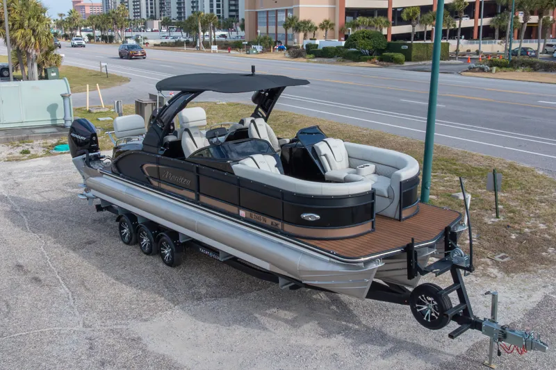 Slide: The Image of 2024 Manitou 25 LX SRW Dual Engine pontoon boat on trailer, parked roadside. - 12