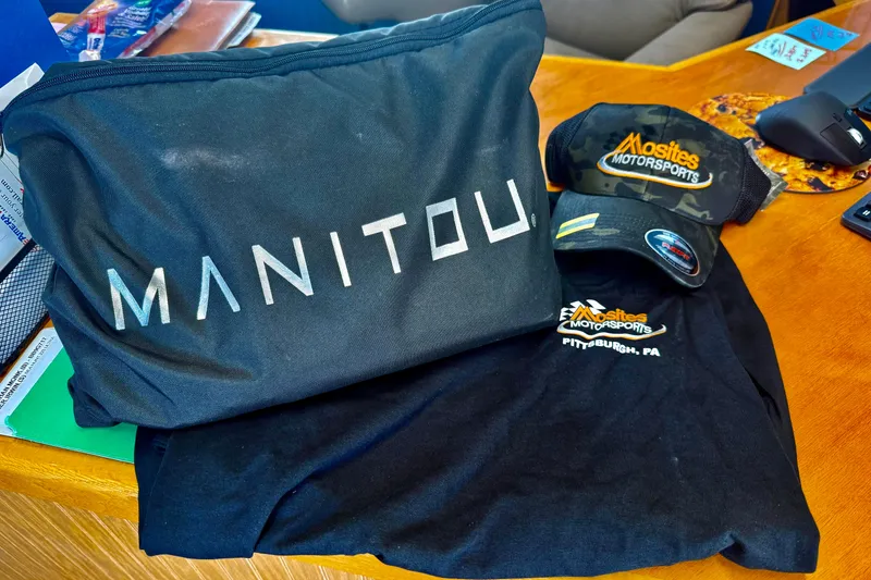 Slide: The Image of Promotional items featuring Manitou branding and Mosites Motorsports apparel on a wooden table. - 9