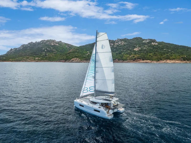 Slide: The Image of 2025 Lagoon 38 catamaran sailing near a scenic coastline under a clear blue sky. - 3