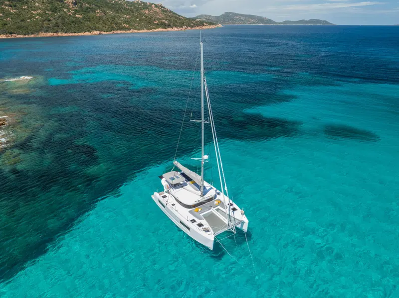 Slide: The Image of 2025 Lagoon 38 catamaran sailing in clear turquoise waters near a rocky coastline. - 70