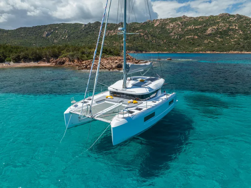 Slide: The Image of 2025 Lagoon 38 catamaran anchored in clear turquoise waters near a rocky coastline. - 71