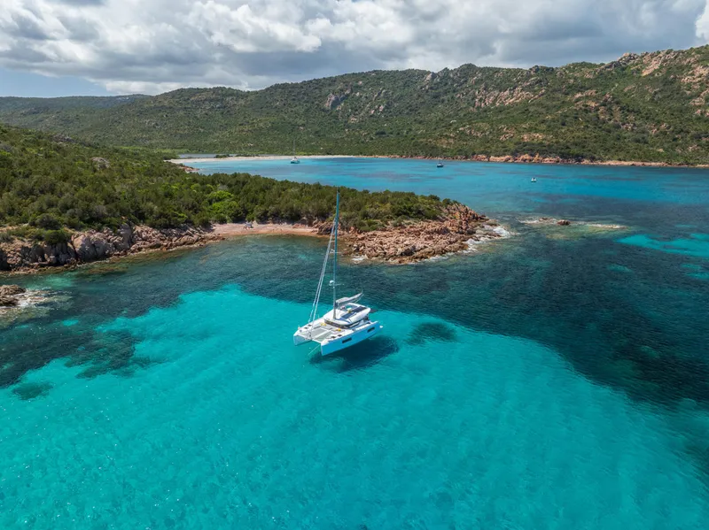 Slide: The Image of 2025 Lagoon 38 catamaran sailing in clear turquoise waters near a rocky coastline. - 74