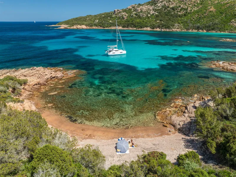 Slide: The Image of A Lagoon 38 catamaran anchored in a serene turquoise bay, surrounded by lush greenery and rocky shores. - 76