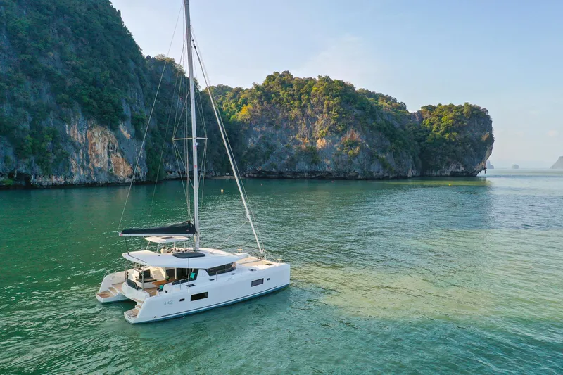 Slide: The Image of 2025 Lagoon 42 Millenium catamaran sailing in scenic, tropical waters near lush cliffs. - 2