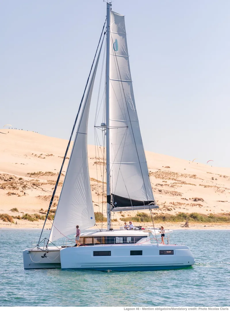 Slide: The Image of 2025 Lagoon 46 ICONIC catamaran sailing near sandy shore under clear blue sky. - 2