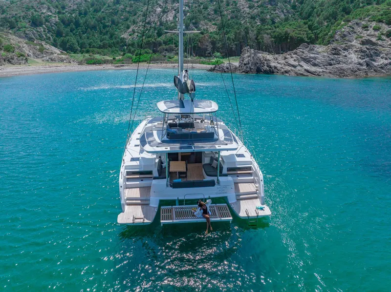Slide: The Image of 2025 Lagoon 51 ICONIC yacht anchored in turquoise waters near rocky coastline. - 14