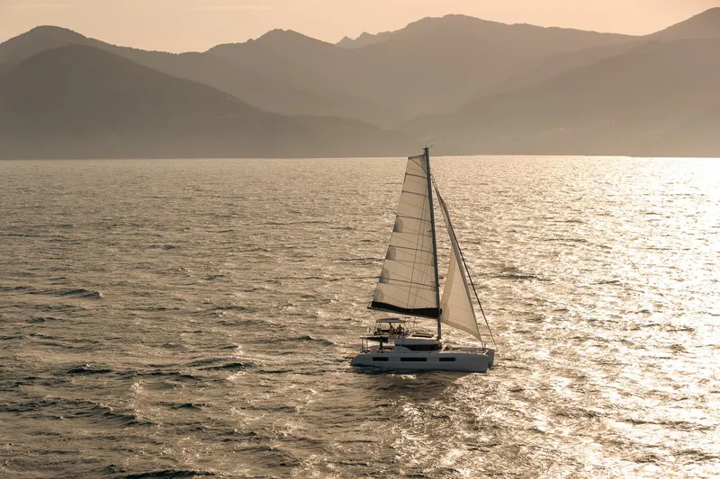 Slide: The Image of Sailing Lagoon 51 ICONIC catamaran on serene waters with mountainous backdrop, 2025 model. - 25