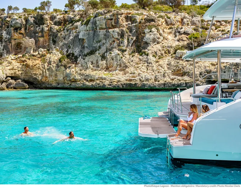 Slide: The Image of Lagoon 55 yacht in turquoise waters near rocky cliffs, 2025 model. - 10