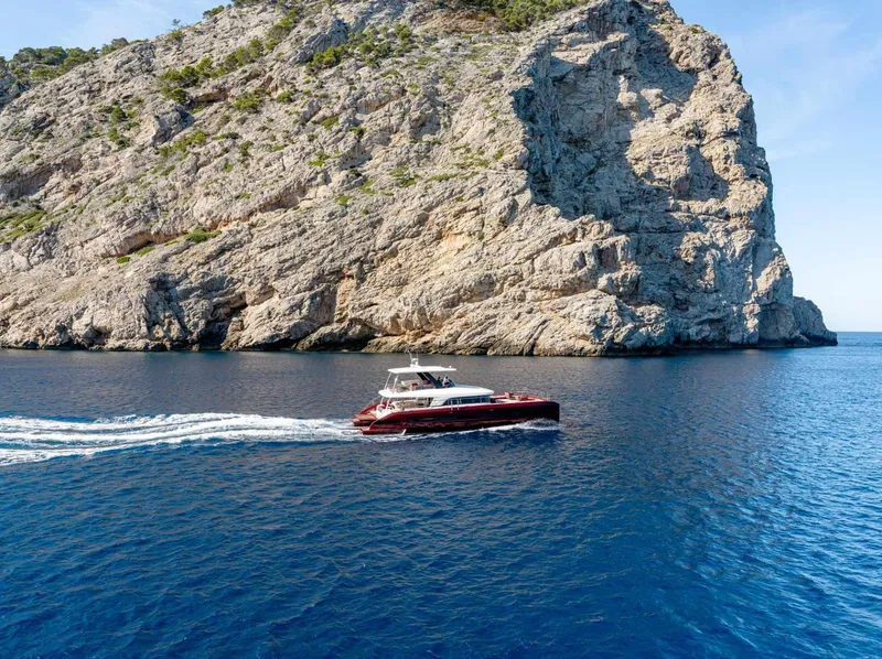 Slide: The Image of 2025 Lagoon SIXTY 7 yacht cruising near a rocky cliff in clear blue waters. - 3