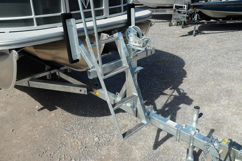 Slide: The Image of Trailer hitch and ladder of 2026 Trifecta 24E CS pontoon boat on gravel surface. - 50