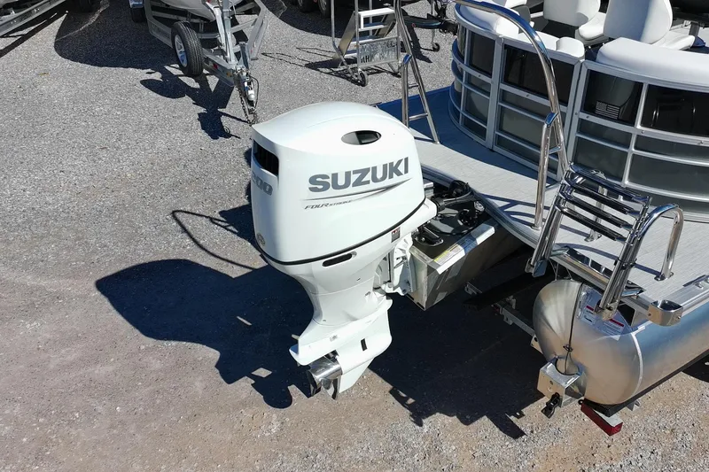 Slide: The Image of 2026 Trifecta 24E CS pontoon boat with Suzuki outboard motor on a gravel surface. - 7