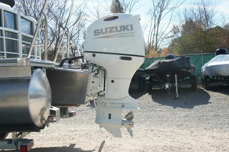 Slide: The Image of 2026 Trifecta 24E CS pontoon boat with Suzuki outboard motor in a storage yard. - 8