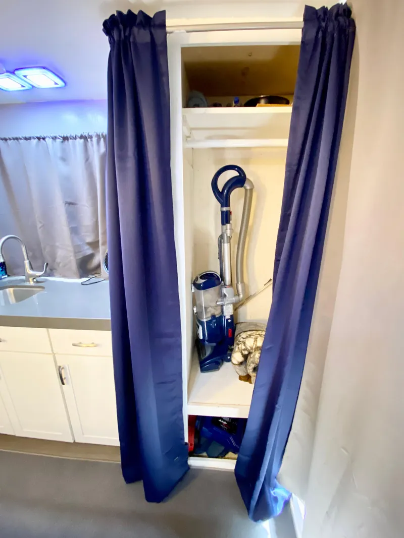 Slide: The Image of 1988 Three Buoys 4412 interior with vacuum in closet, blue curtains, and kitchen sink. - 25