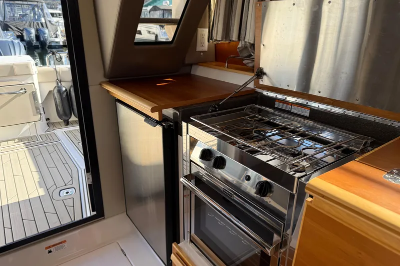 Slide: The Image of 2022 Cutwater C-32 CB boat kitchen with stove, fridge, and wooden countertops. - 23