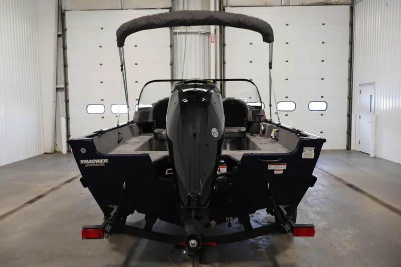 Slide: The Image of 2024 Tracker Pro Guide V-16 WT boat in a garage, rear view with motor. - 6