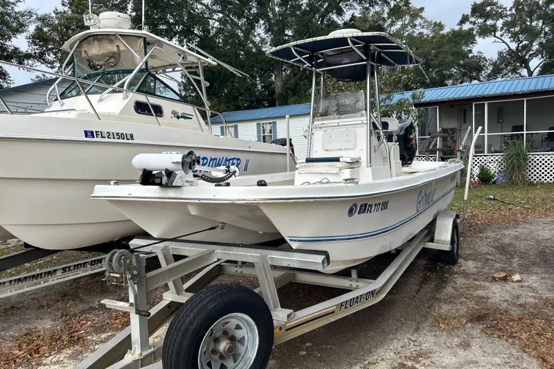 Slide: The Image of 2017 Twin Vee 22 BayCat boat on trailer, parked beside another boat, near a house. - 2