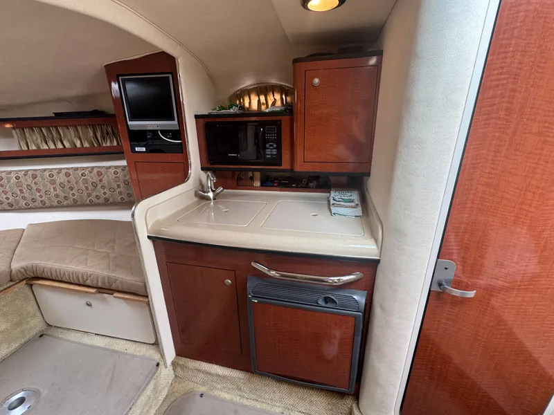 Slide: The Image of The cabin of a 2005 Sea Ray Sundancer 280 features a compact kitchen with wood cabinets and a small fridge. - 7
