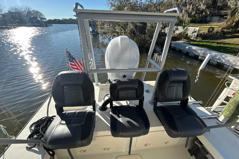 Slide: The Image of 2024 Custom Florida Flats CC boat with three black seats, docked by a scenic river. - 16