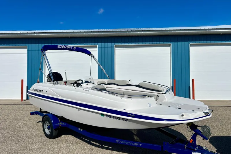 Slide: The Image of 2018 Starcraft 2000 OB Limited boat on trailer, parked outside blue garage. - 2