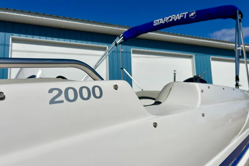 Slide: The Image of 2018 Starcraft 2000 OB Limited boat with blue canopy, parked near a blue building. - 59