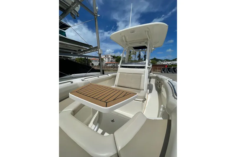 Slide: The Image of 2021 Boston Whaler 230 Outrage boat interior with seating and table under a clear blue sky. - 5