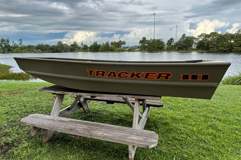 The Image of 2026 Tracker Grizzly 10 Jon boat displayed on a picnic table by a lake. - 0