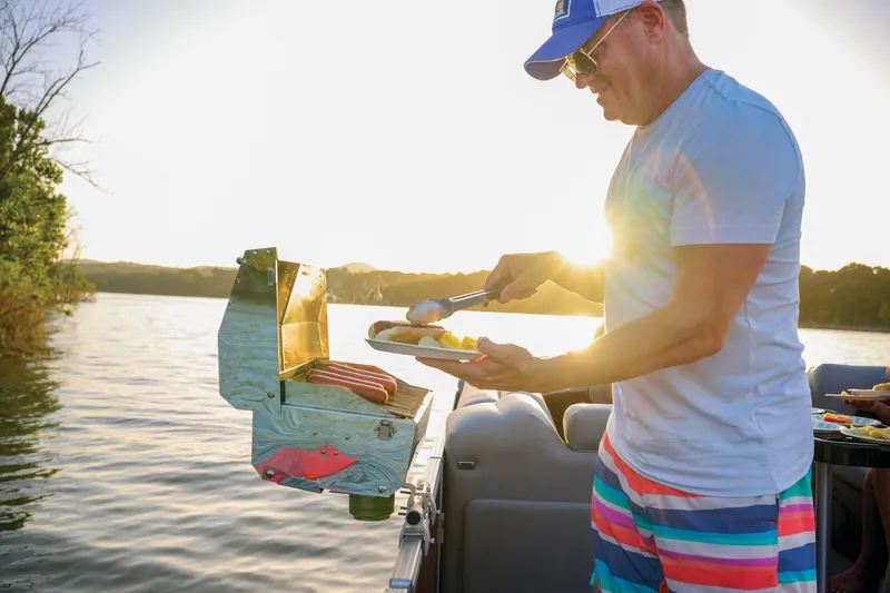 Slide: The Image of Manufacturer Provided Image: Man grilling on 2026 Sun Tracker Party Barge 22 DLX at sunset. - 11