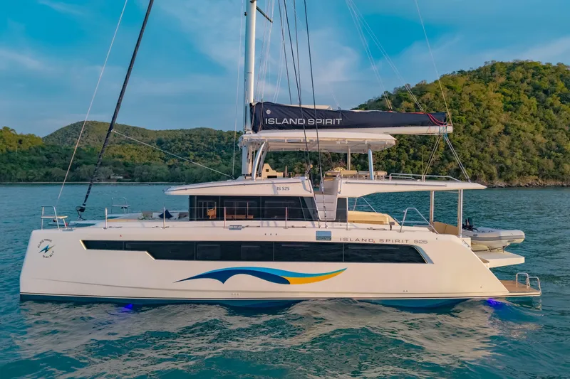 Slide: The Image of 2026 Island Spirit 525E catamaran sailing on serene waters near lush green hills. - 7