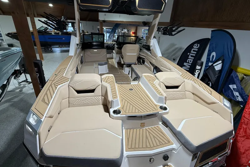 Slide: The Image of 2025 MasterCraft XStar 23 boat interior with beige seating and wood accents in showroom. - 2