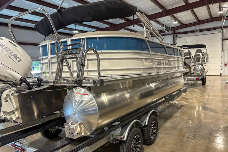 Slide: The Image of 2025 Trifecta 20RF LE pontoon boat in showroom with Suzuki outboard motor. - 2