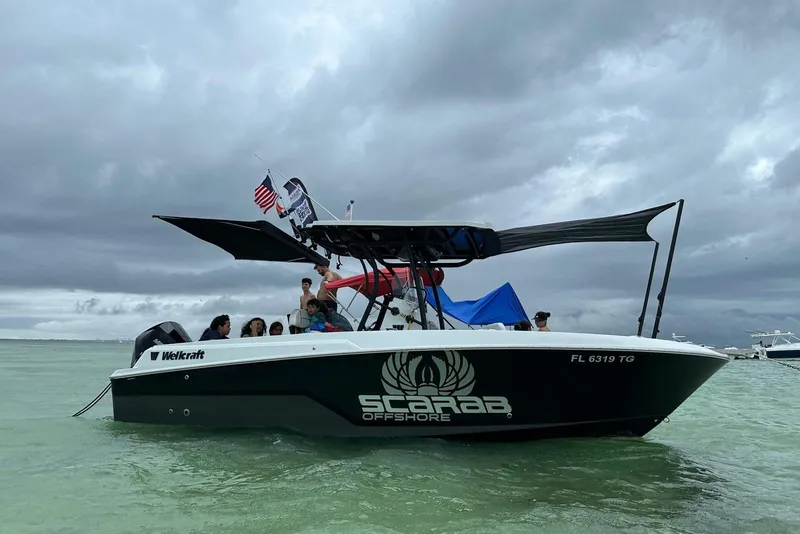 The Image of 2022 Wellcraft 222 Fisherman boat on water, cloudy sky, people onboard, Scarab Offshore branding. - 1