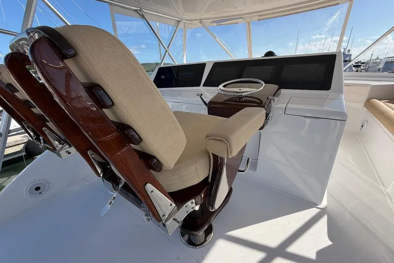 Slide: The Image of Captain's chair and helm of 2004 Viking 56 Convertible yacht, featuring elegant wood and beige upholstery. - 59