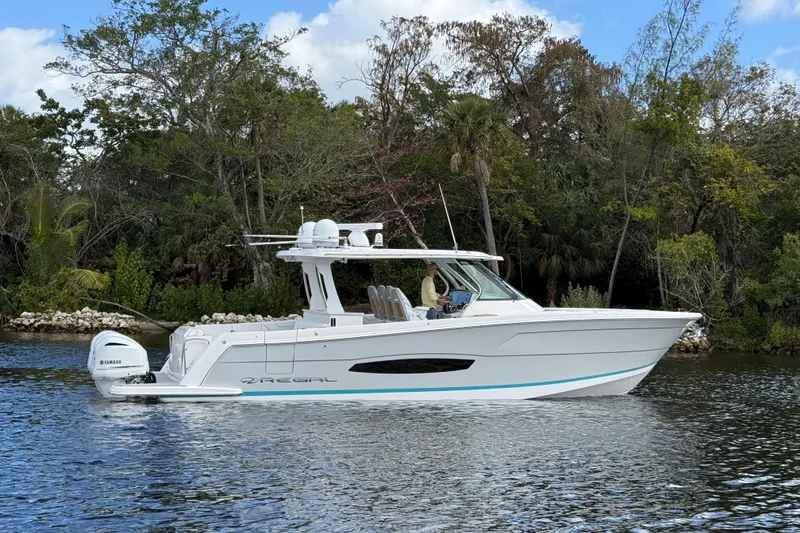 Slide: The Image of 2020 Regal 38 SAV boat cruising on a calm river with lush greenery. - 2