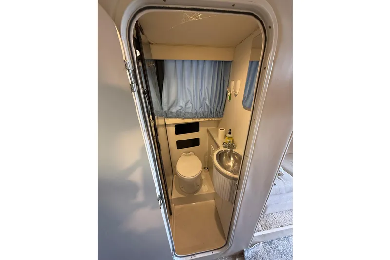 Slide: The Image of 1994 Carver 320 Voyager bathroom with toilet, sink, and blue curtains. - 13