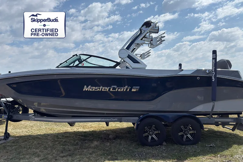 The Image of A 2022 MasterCraft XT24 boat on a trailer in a grassy area. It is certified pre-owned. - 0