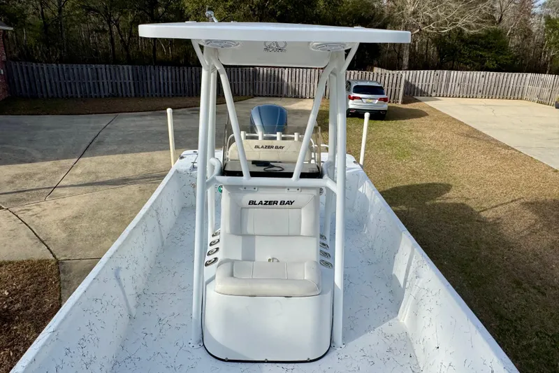 Slide: The Image of 2017 Blazer Bay 2400 boat with T-top, parked in driveway, surrounded by trees. - 8