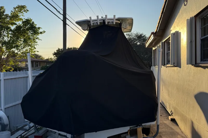 Slide: The Image of 2018 Robalo R242 Center Console boat covered, parked beside a house at sunset. - 21