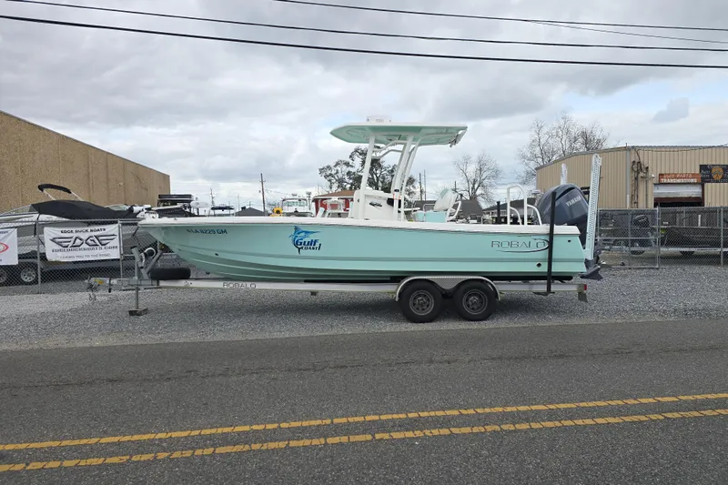 Slide: The Image of 2021 Robalo 246 Cayman boat on trailer, parked outdoors near industrial buildings. - 6