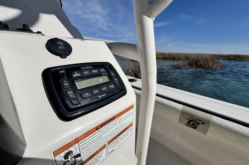 Slide: The Image of 2022 Carolina Skiff 24 Ultra Elite boat console with audio system, near water and reeds. - 3