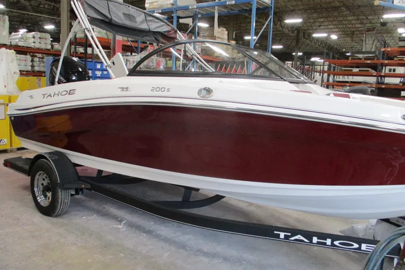 The Image of 2024 Tahoe 200 S boat in warehouse, red and white design on trailer. - 0
