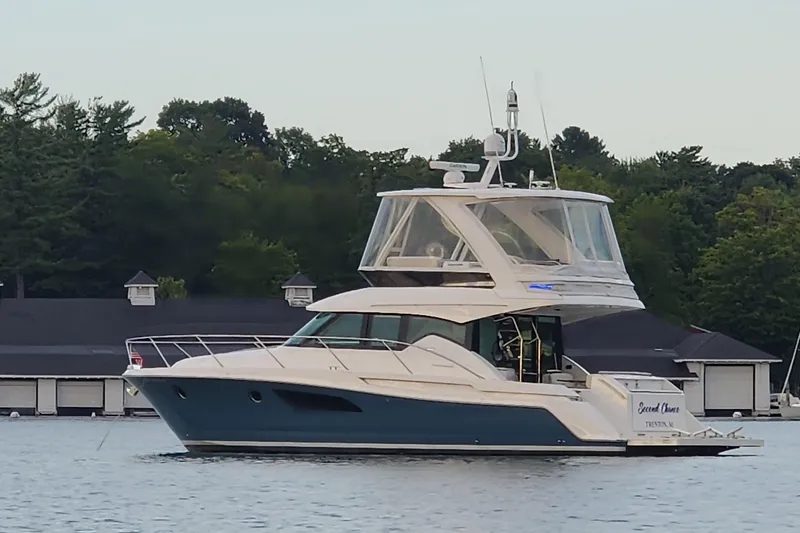 Slide: The Image of 2020 Tiara Yachts F44 Flybridge on calm water near marina, surrounded by trees. - 4