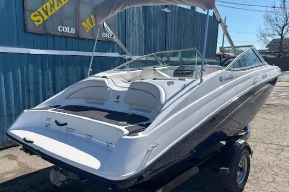 Slide: The Image of 2012 Yamaha Boats SX190 on trailer, parked outdoors near blue building. - 2